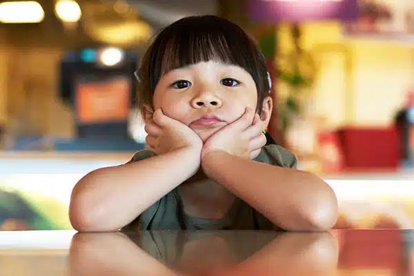 Cognitive development and pandemic effect on children, featuring a young child sitting at a table looking bored.