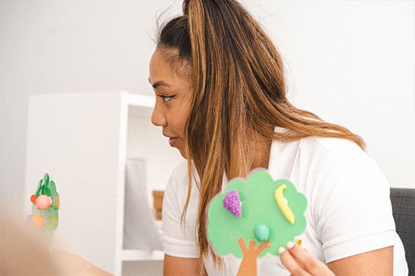 Children's Image Training Activities through visualisation games, featuring a Shichida teacher holding a tree cutout with plastic fruit pasted onto it, prompting kids to use their imagination