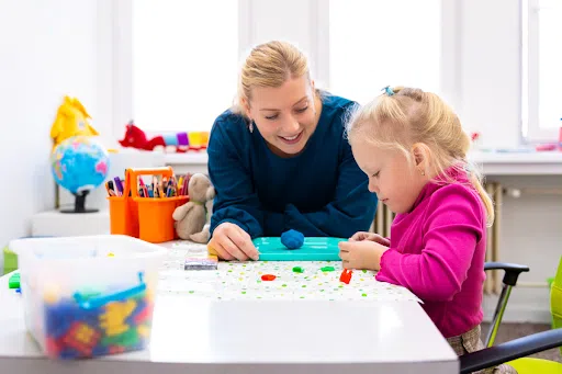 An adult watching a child play with play dough
