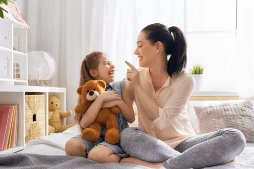 Mum, child and a teddy bear on a bed, engaging in play