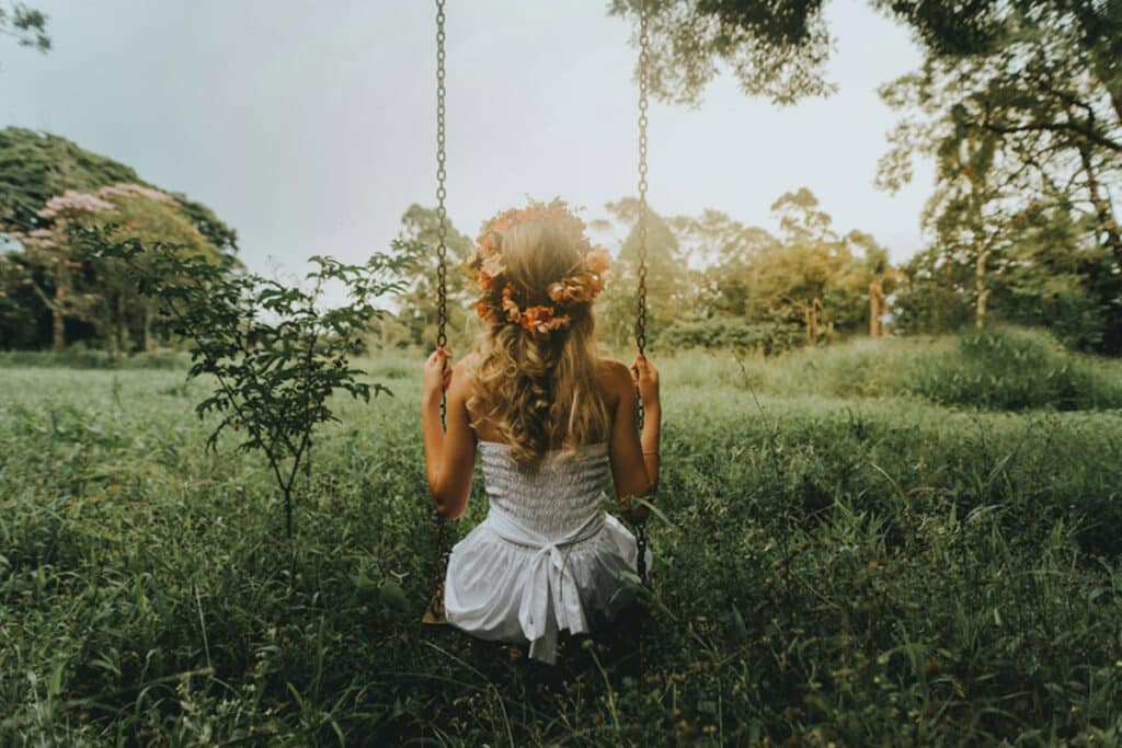 A girl sitting on a swing in a beautiful nature setting, her back is turned towards the camera as she sits on the swing.