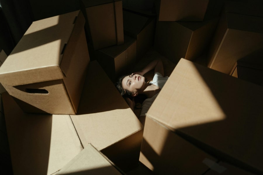 A woman lies under a pile of moving boxes