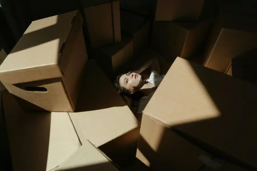 A woman lies under a pile of moving boxes