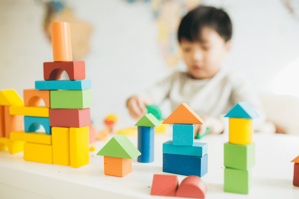 A young boy is playing with building blocks, and has built some block towers