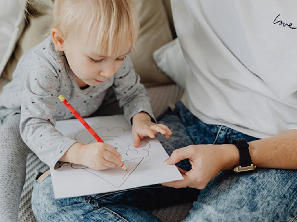 A toddler drawing on her father's lap, drawing is great for brain development