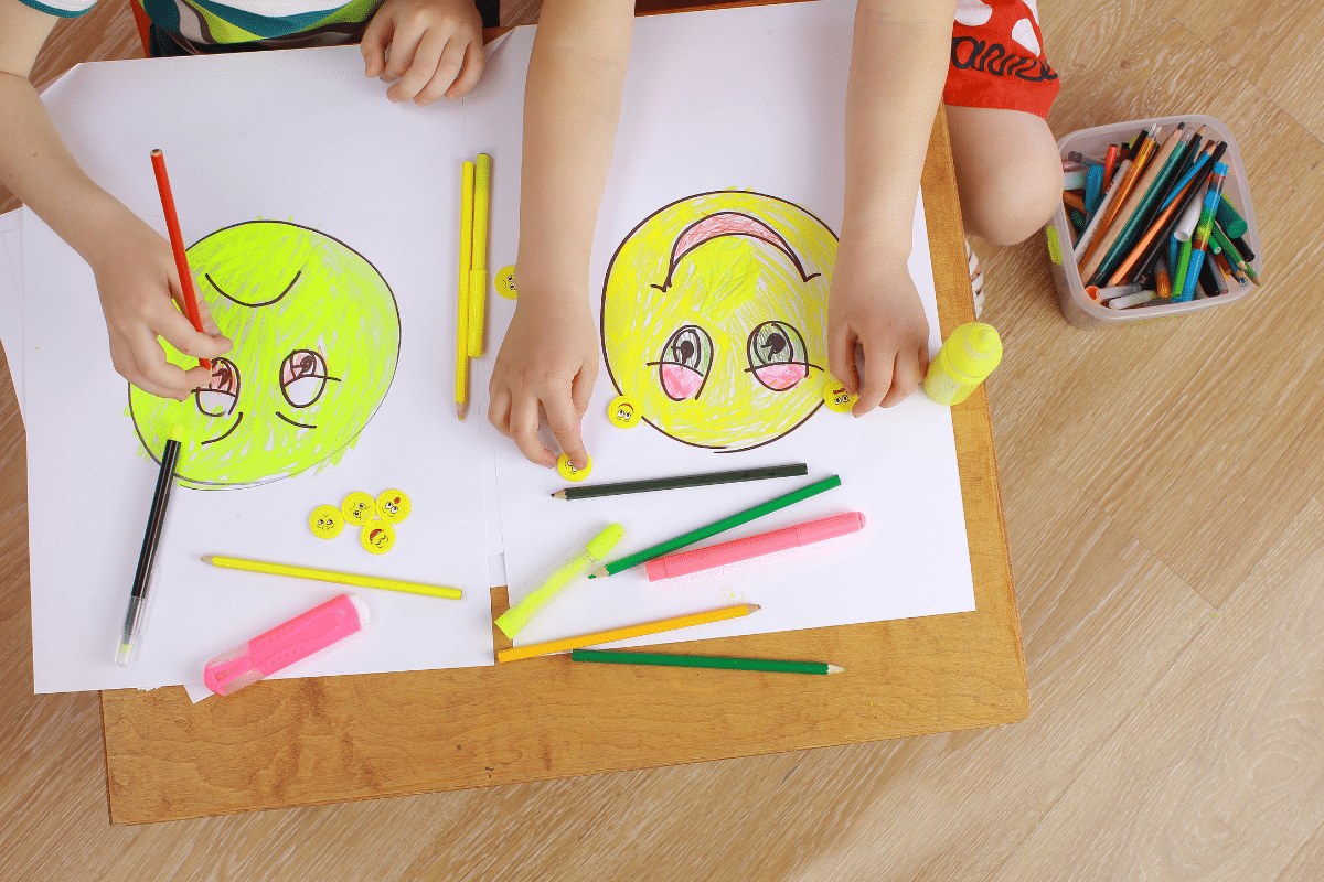 Two kids drawing faces, one face is happy and one is sad