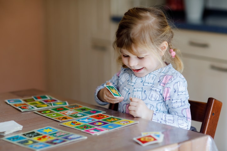 Excited smiling toddler girl playing a picture card game. Happy healthy child training memory, critical thinking, family activity at home.