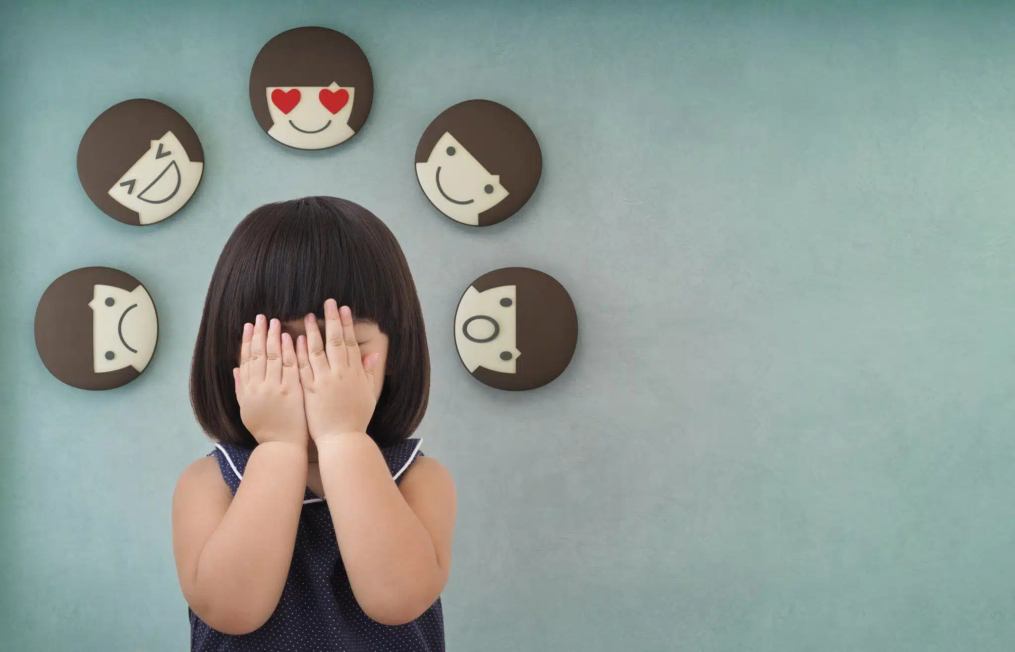 Emotional Regulation Activities for Kids, featuring a child hiding her face, with little comical faces around her hear, showing a variety of emotions.