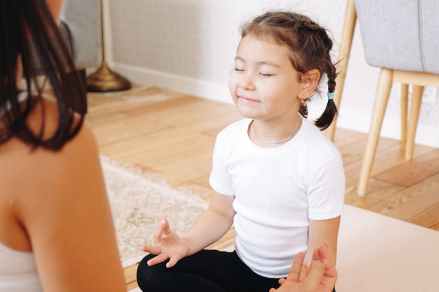 Kids mental health, here a preschooler is doing meditation with her mum at home.