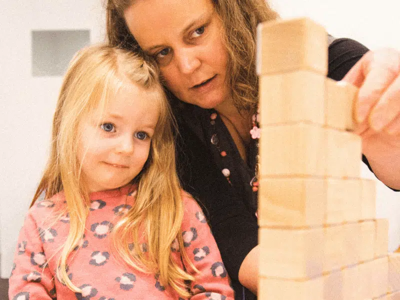 Kids mental health is improved by spending quality time with trusted adults. Here a mum and child play a game together, building blocks together.