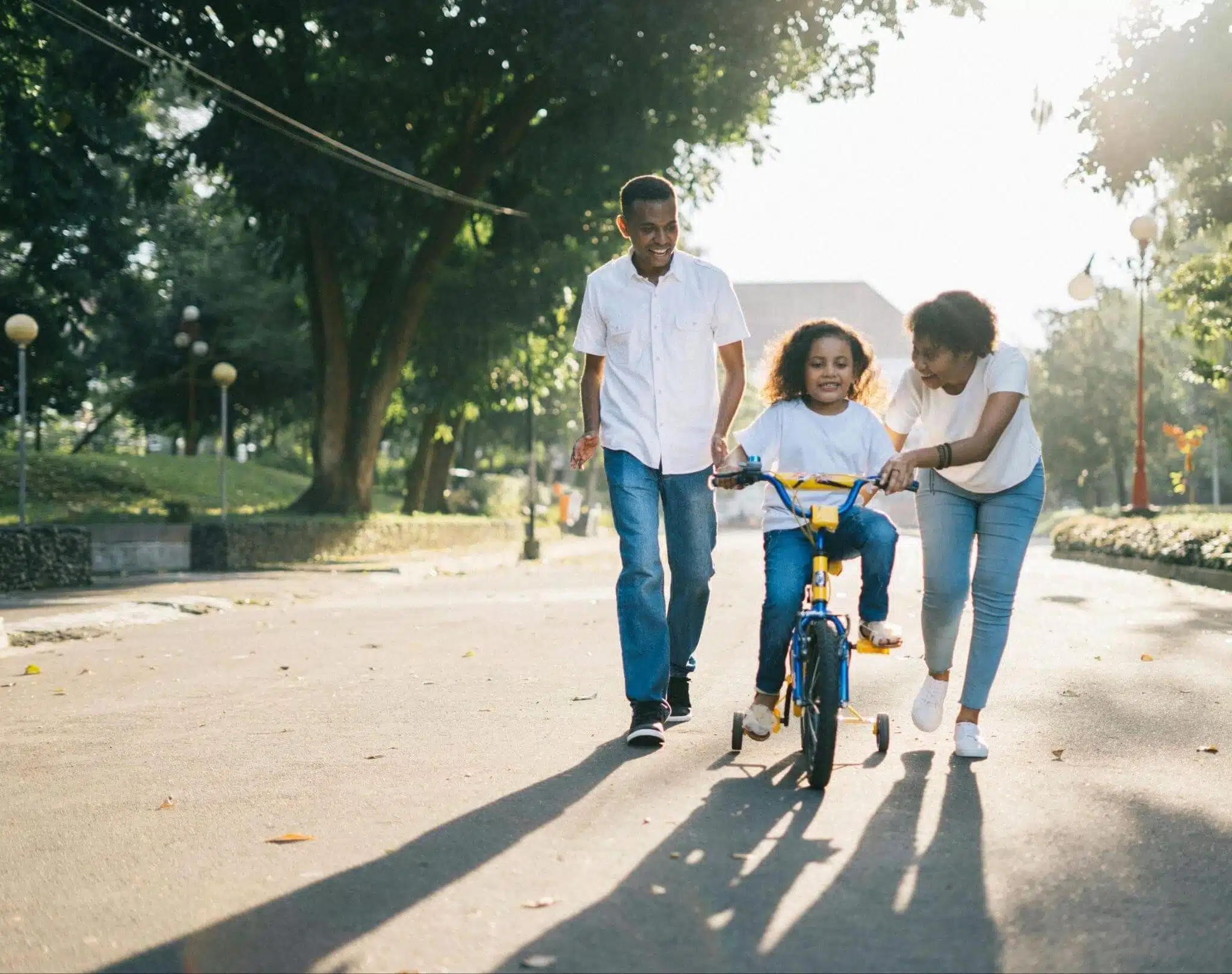 Building balance and confidence with coordination exercises during early childhood is crucial for your child’s development, here a mum and dad help a preschooler ride a bike.