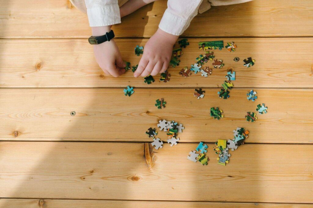 A child sits on a wooden floor, focused on assembling colorful puzzle pieces scattered around them. Puzzles are great for neuroplasticity exercises.