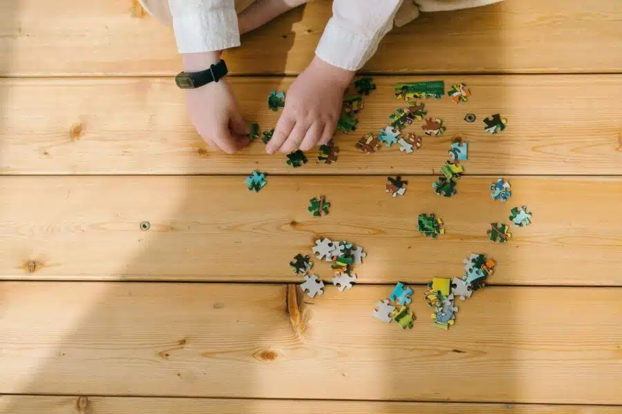 A child sits on a wooden floor, focused on assembling colorful puzzle pieces scattered around them. Puzzles are great for neuroplasticity exercises.