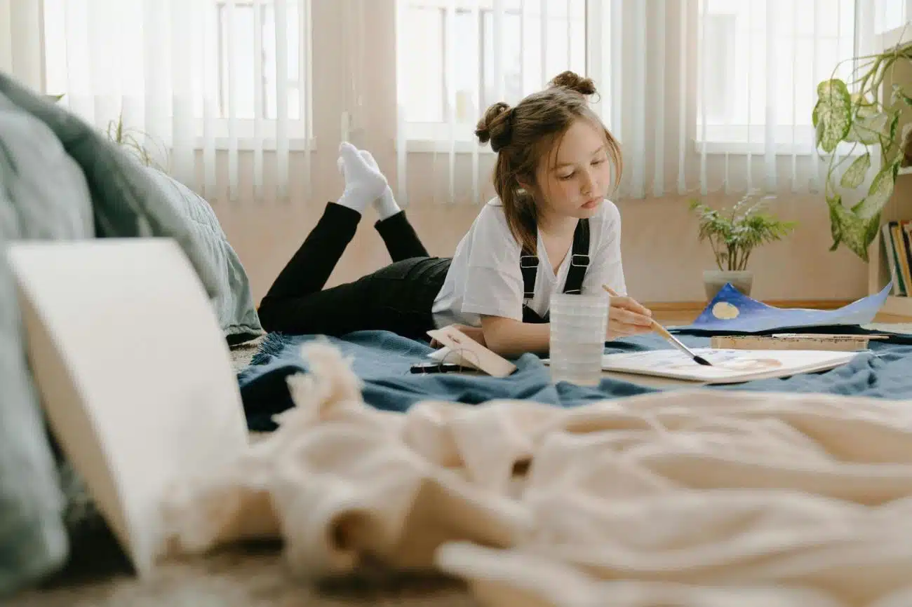 Fun activities for kids - Kid in White shirt painting while lying on her stomach,