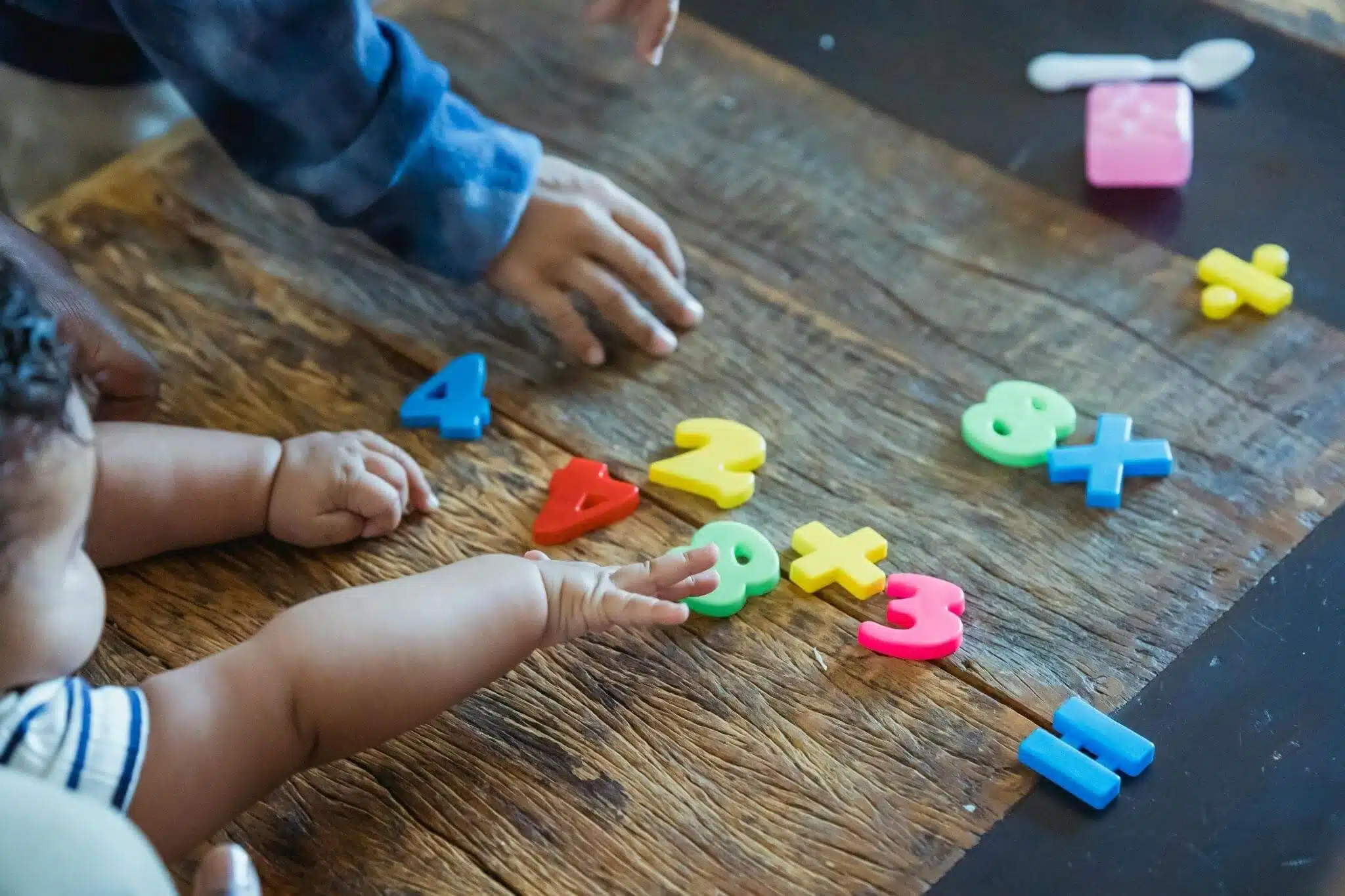 Two children are playing with colorful plastic numbers on a table, engaging in a fun educational activity, which can be seen in our early numeracy skills checklist.