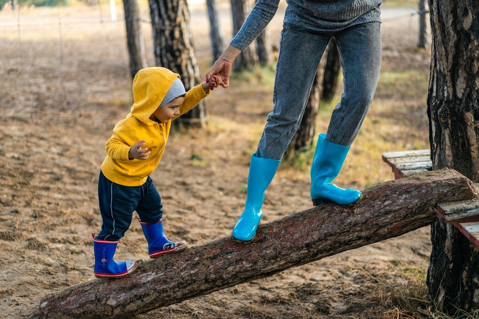 Parent Helping Child in Yellow Jacket to Walk on Sloped Wood