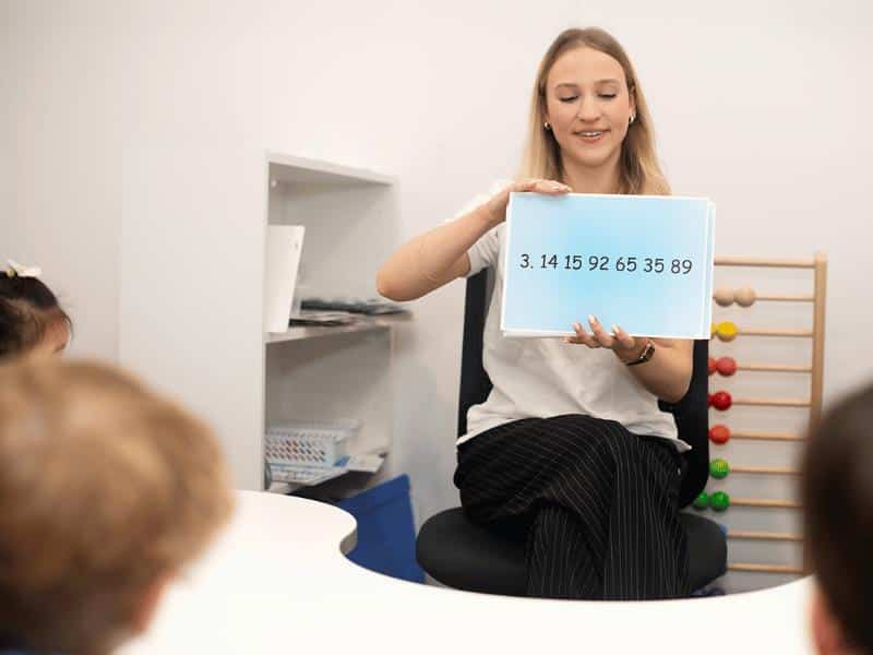 Learning the digits of Pi using song and flashcards strengthens visual, auditory, and working memory. Here a Shichida teacher holds up flashcards, singing the pi song along with the kids.