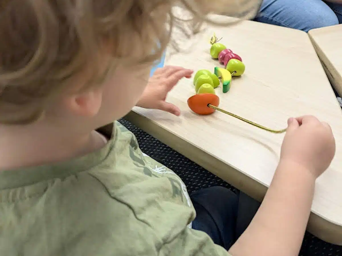 A toddler threading large beads