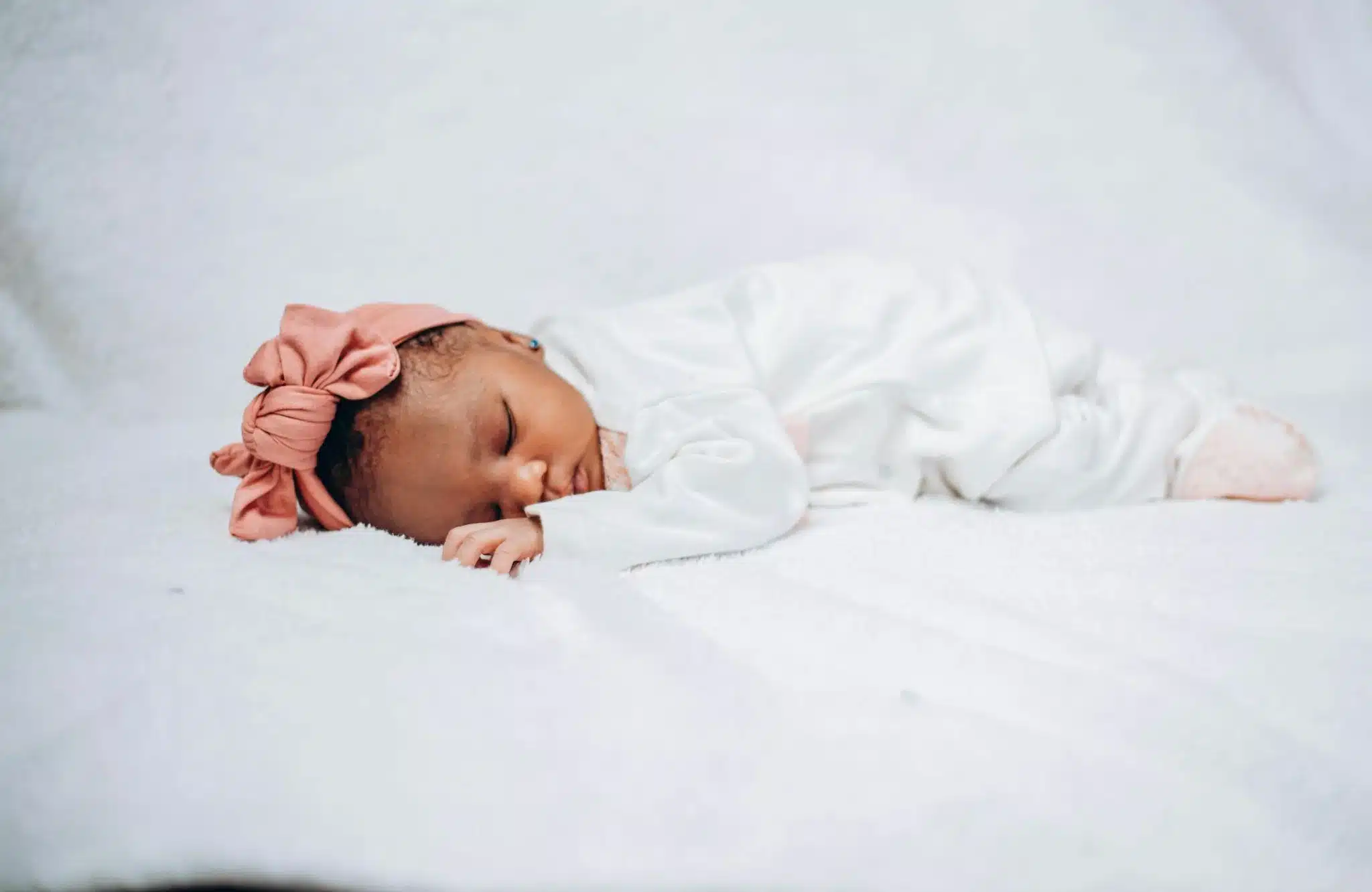 Peacefully sleeping newborn baby wearing a pink bow headband.