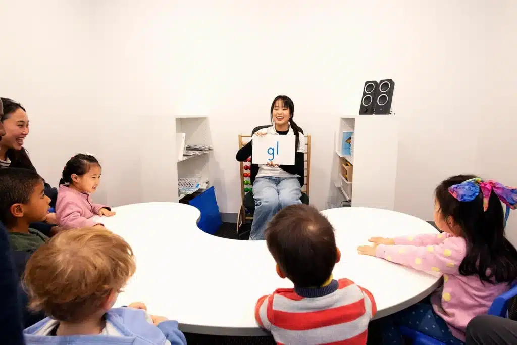 Teacher holding a phonics letter card in front of preschoolers seated around a round table